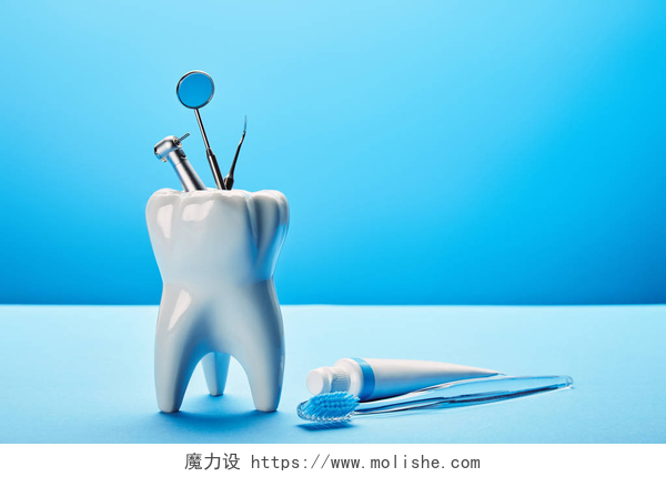 蓝色背景上牙齿模型和牙科器械在蓝色背景下, 可近距离查看白色牙齿模型、牙刷、牙膏和不锈钢牙科器械